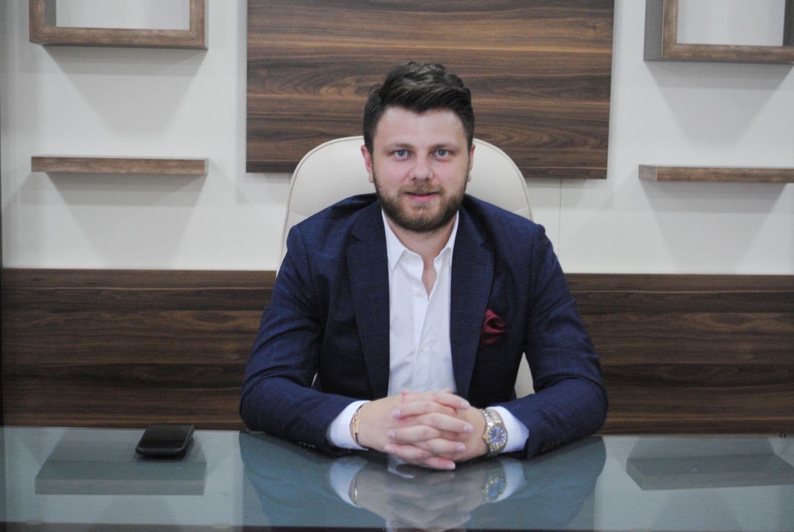 Ömer Yazıcıoğlu, ahşap kaplamalı bir ofiste cam masasının başında